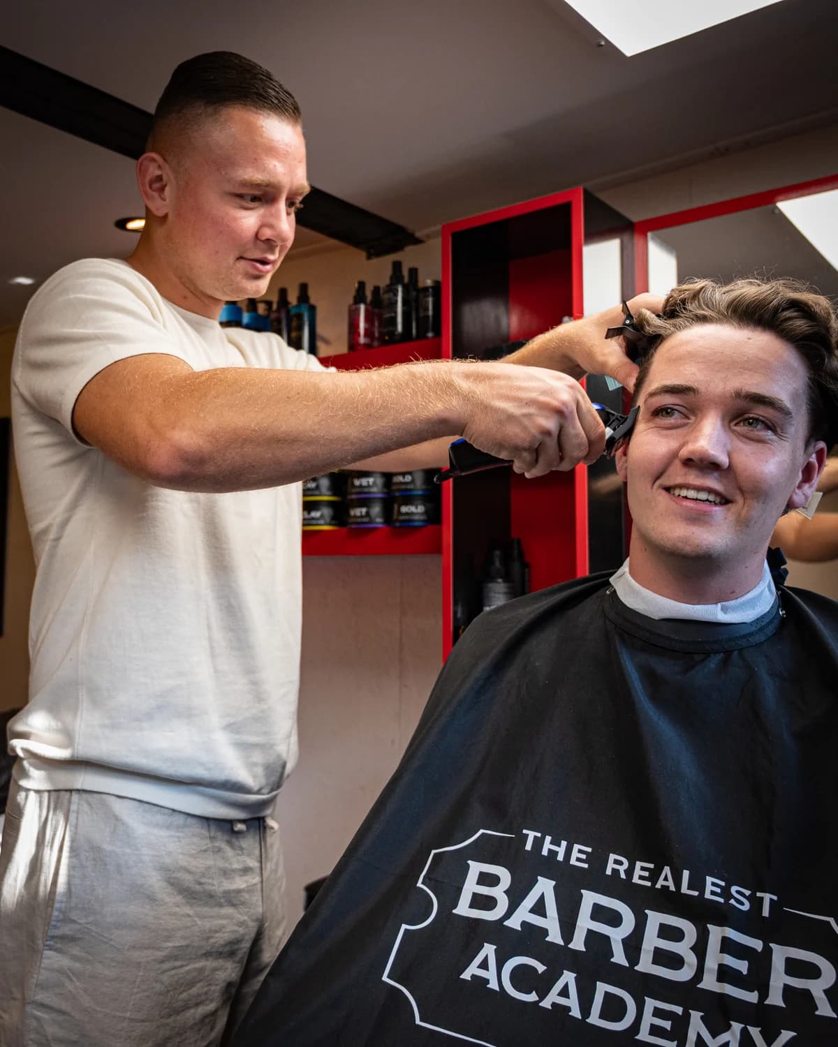 Vincent werkt met de tondeuse terwijl de klant in de stoel glimlacht